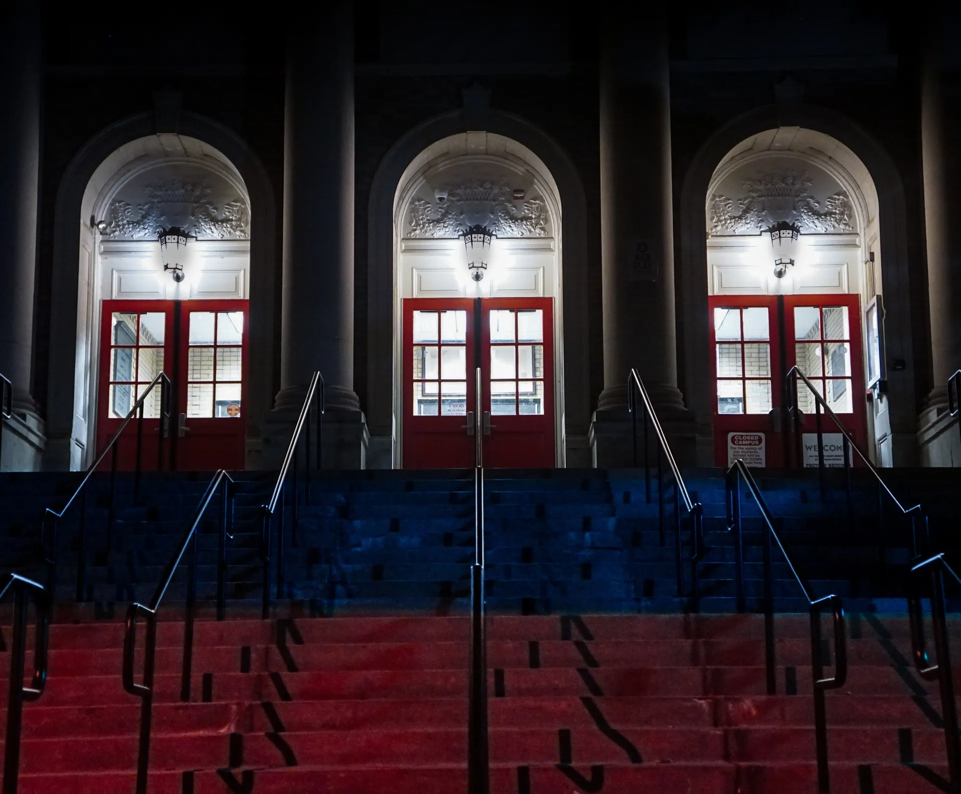 Three symmetrical arched entryways with glowing red doors atop a blue and red lit staircase